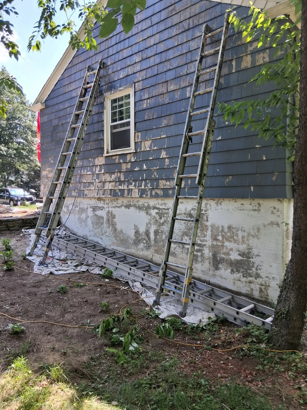 Blue shingle siding being prepared for painting with ladders in place